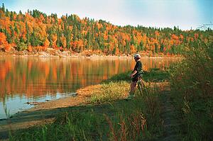 Cyclist taking a break by river in autumn