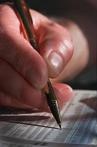 Closeup of man's hand and pen circling Investment in newspaper