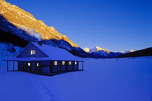Cottage in heavy snowfall with sunrise on mountain in background