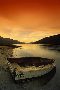 Old rowboat at water's edge with sunset background