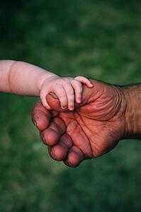 Closeup of baby's hand holding thumb of man's rough hand