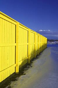 Bright yellow fence with blue sky and snow