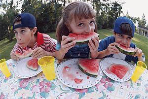 Three children eating watermelon at a picnic table