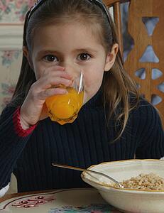 Young girl drinking orange juice at breakfast table