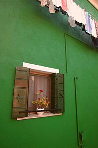Flowers displayed on window sill of a colourful home with laundry hanging to dry on the Island of Burano Venetian Lagoon Italy