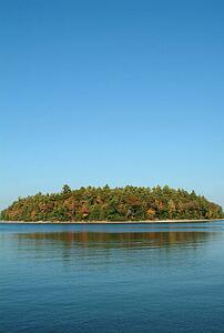 A forested island in a lake against a blue sky and blue water