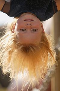 Young girl hanging upside down in the playground on an autumn day