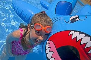 Girl playing in swimming pool with inflatable shark