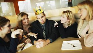 Man with flimsy crown on head and women paying attention to him