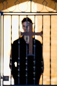 Man standing behind iron fence with cross