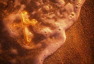 Cross being washed over by wave on sandy beach