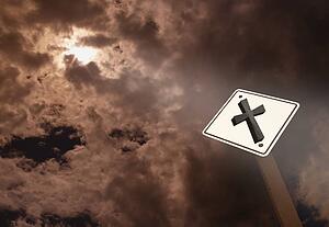 A road sign with a cross against a cloudy sky