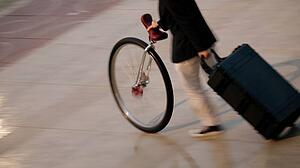 A person pushing a unicycle and pulling a suitcase