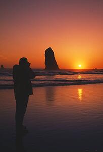 Silhouette of person viewing sunset, rock formation, Cannon Beach.