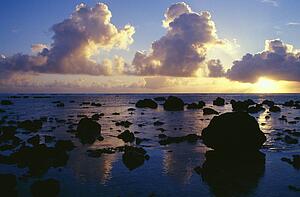 Reflected sunset, clouds, and silhouetted rocks on beach, Rarotonga Island.