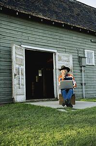 Man in cowboy hat working on computer outside of barn