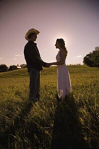 Young man and woman in field holding hands