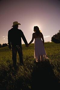 Man and woman walking hand-in-hand in field in sunset