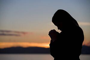 A teenage girl prays at sunset
