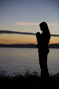 A teenage girl prays at sunset by the ocean.