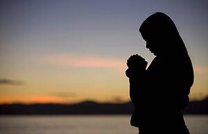 A teenage girl prays at sunset by the ocean.