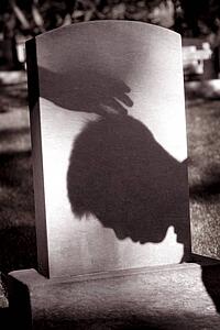 Shadow of hand over head of grieving man at grave site