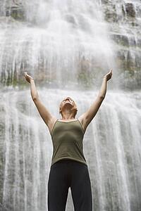 Woman with arms raised in front of waterfall