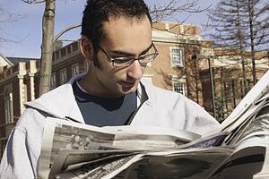 Young man reading newspaper outside