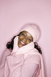 Portrait of smiling African-American mid-adult woman on pink background wearing winter coat, hat, and scarf.