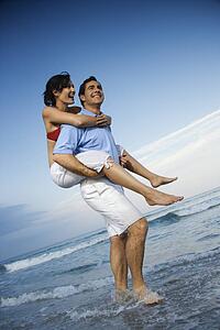 Caucasian mid-adult male carrying female piggyback style on beach.