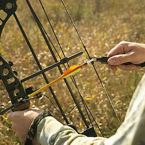Bow hunter hands holding compound bow in field.