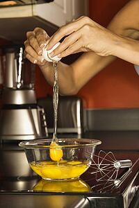 Close-up of young adult woman's hand cracking open an egg into a bowl.