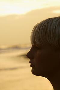 Profile of caucasian pre-teen boy on beach at sunset.