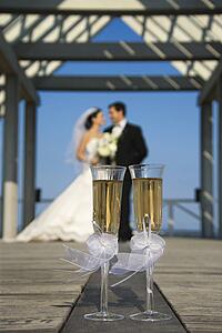 Pair of flute glasses of champagne with Caucasian bride and groom blurred in background.