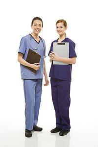 Portrait of Caucasian women doctors in medical scrubs standing holding medical charts against white background.