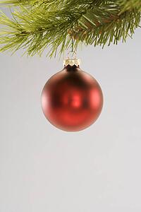 Still life of red Christmas ornament hanging from pine branch.