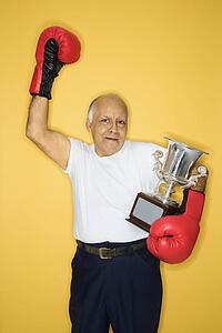 Caucasian mature adult male holding trophy and wearing boxing gloves.