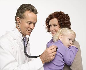 Middle-aged adult Caucasian male doctor holding stethoscope to female toddler's back with mother watching.