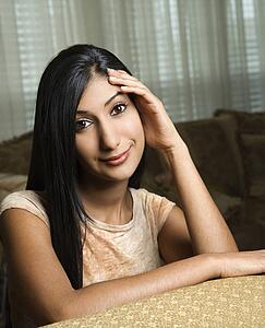 Close up portrait of Asian/Indian young woman sitting on couch.