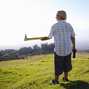 Pre-teen Caucasin male holding remote control and airplane standing on a grassy knoll.