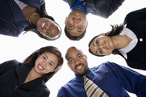 Low angle portrait of multi-ethnic business group of men and women in huddle looking at viewer.