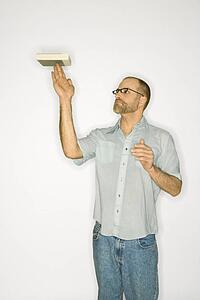 Caucasian man balancing book on fingers standing against white background.