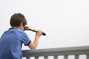 Caucasian pre-teen boy leaning on railing looking through telescope.