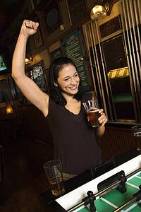 Young Caucasian woman smiling and cheering on foosball game.