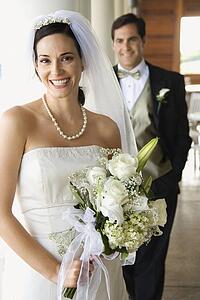 Caucasian mid-adult bride and groom standing on porch looking at viewer and smiling.