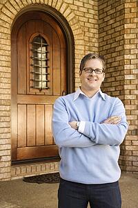 Caucasian adult male standing with arms crossed near arched doorway. 