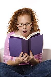 Caucasian female child sitting reading book looking surprised.