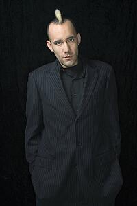Portrait of Caucasian man in suit with mohawk against black background.