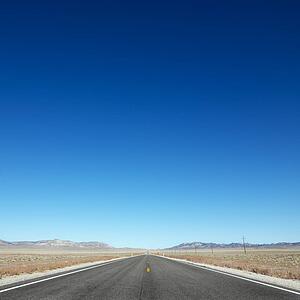 Strip of highway stretching towards horizon under clear blue sky.