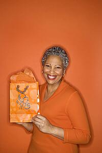 African American mature adult female holding gift bag smiling.